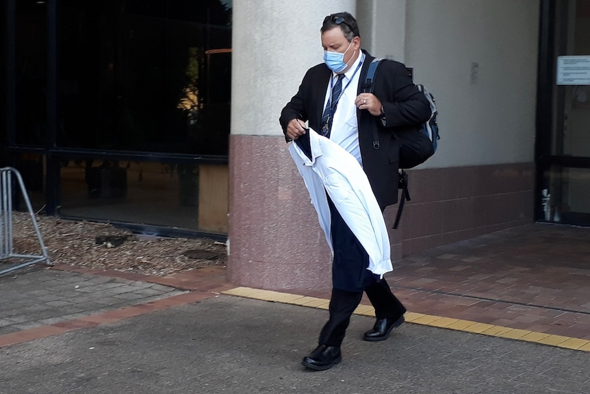 A man in a suit and face mask leaves a courthouse