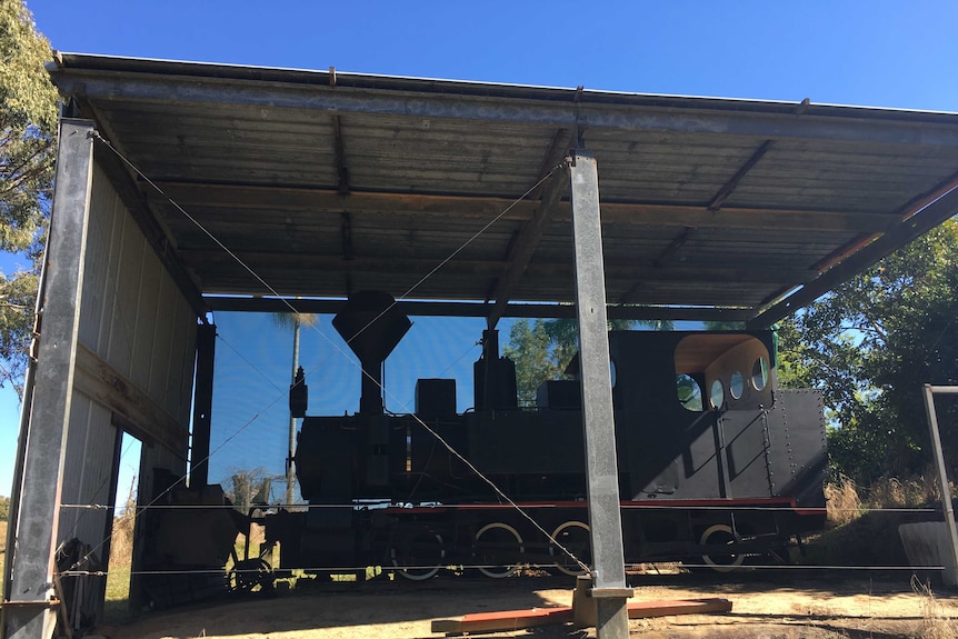 A small locomotive under a shed on a rural property.