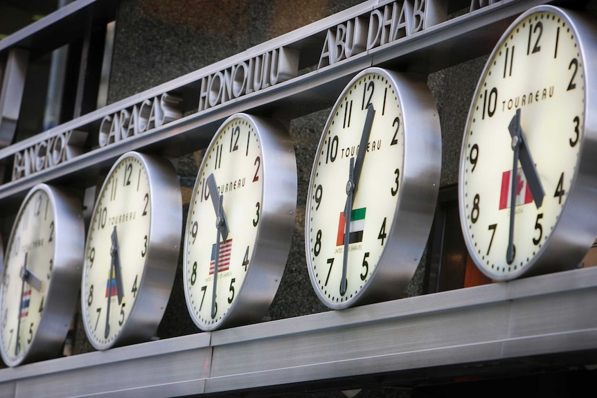 A row of clocks outside of a building showing different times from around the world.