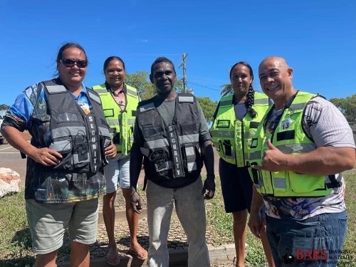 Five people smile at camera with security vests on. 