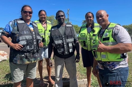 Five people smile at camera with security vests on. 