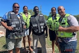 Five people smile at camera with security vests on. 