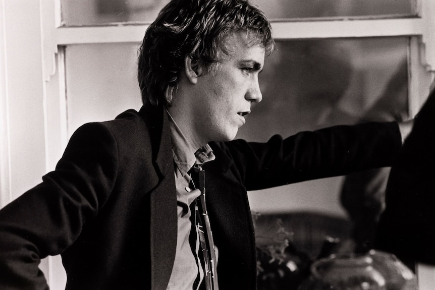 Young Cold Chisel drummer wears a suit leaning his hand against a wall