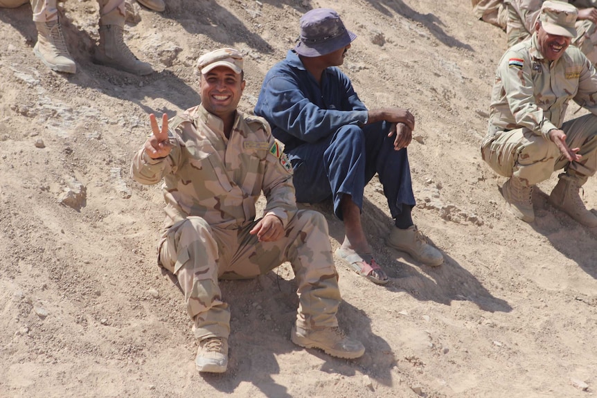 A soldier throws a peace sign while sitting in the sand.