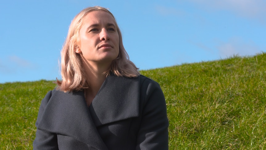 A woman sits on a grassy hill.