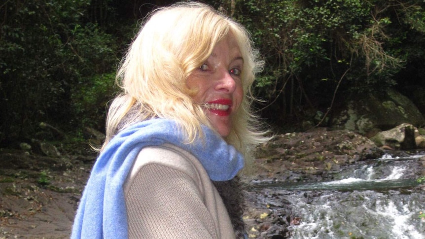 Smiling Maureen Boyce stands by a stream in a forest, date unknown