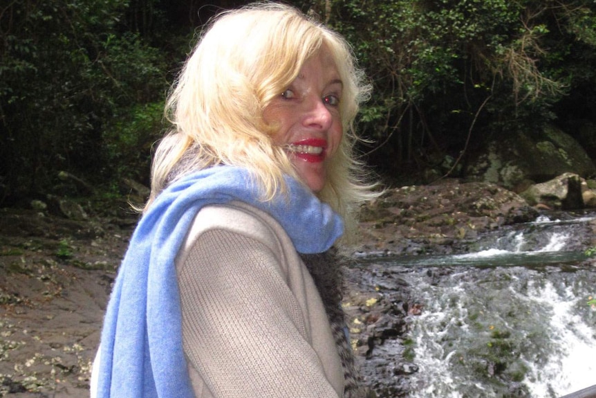 Smiling Maureen Boyce stands by a stream in a forest, date unknown
