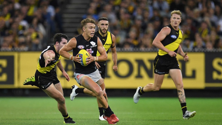 An AFL player bursts through the middle as an opponents reaches out to try to tackle him.