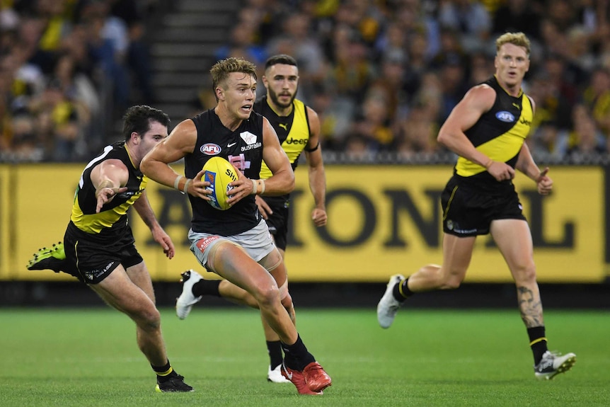 An AFL player bursts through the middle as an opponents reaches out to try to tackle him.