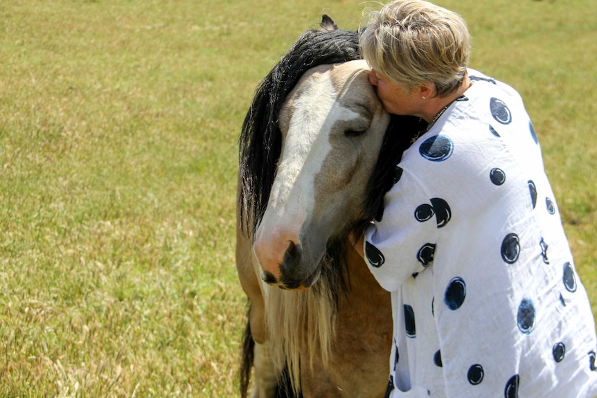 Woman standing in a paddock and kissing the brow of her horse.