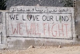 The words "We Love Our Land, We Will Fight" are painted on a grey brick wall in Palestinian village Kafr Qaddum.