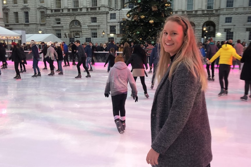 A woman ice skating on a crowded rink, a Christmas tree in the background