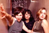Sleater-Kinney's Carrie Brownstein, Janet Weiss and Corin Tucker standing in a narrow passageway looking directly to camera