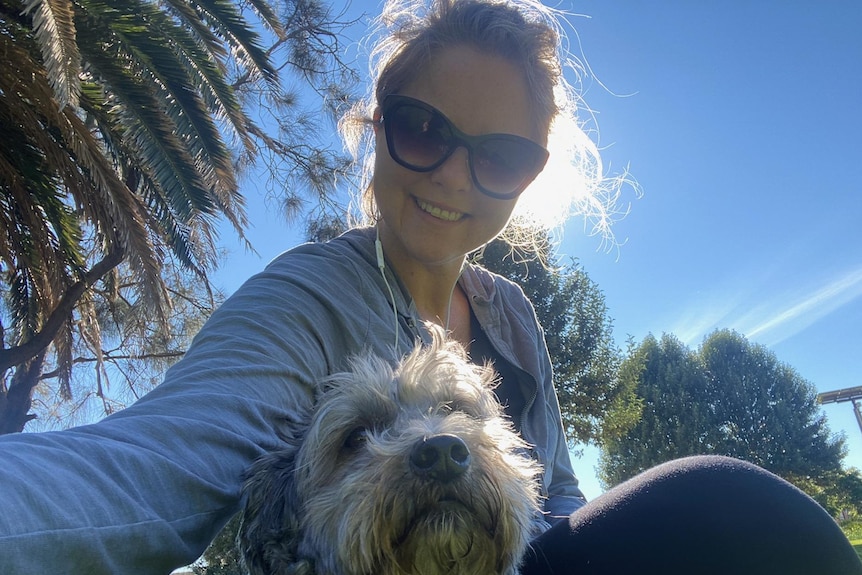 A selfie of a smiling woman posing with her dog with the sun behind. 