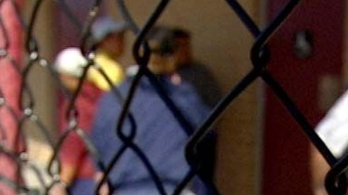 Prisoners standing behind fence at prison