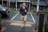 Chris May crosses the street holding a coffee cup