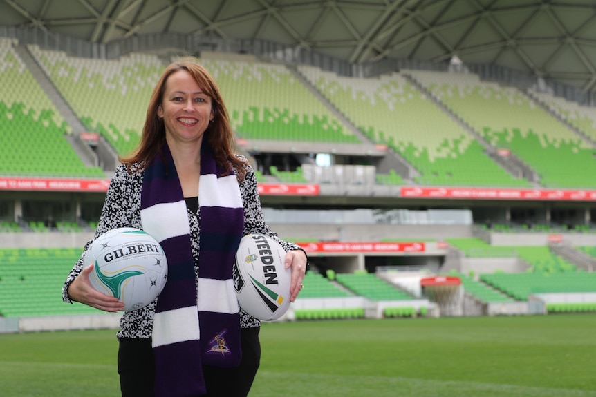 Smith poses for a photo at AAMI Park with a netball and rugby league steeden