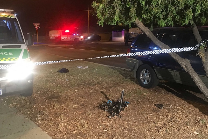 The mangled wreckage of a bicycle on a street verge at night surrounded by an ambulance, police tape and a four-wheel drive.