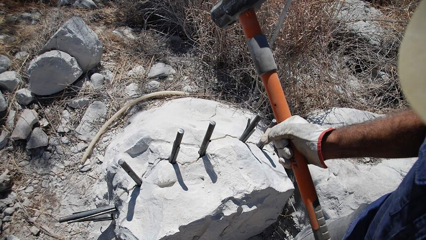 A photo of someone holding a sledgehammer, about to crack open a limestone rock.