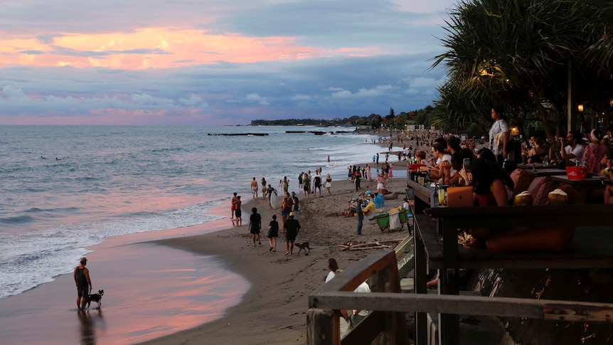 People in beachside bars watch a sun set over the ocean
