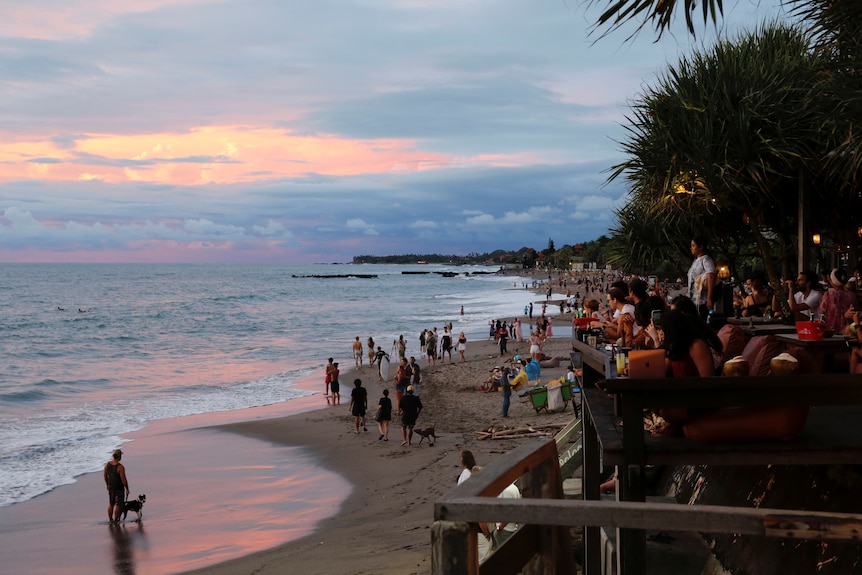 People in beachside bars watch a sun set over the ocean