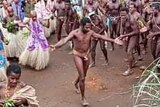A man wearing no clothes except for a covering around his waist dances in the middle of a group of men and women.