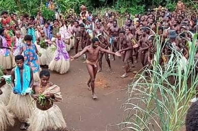 A man wearing no clothes except for a covering around his waist dances in the middle of a group of men and women.