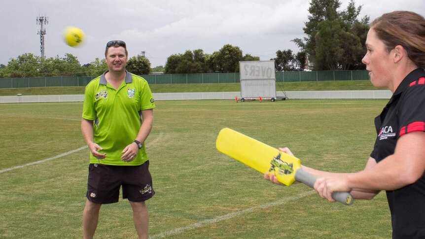 A cricket NSW development officer in a green T20 blast about to take a catch from a woman holding a yellow bat