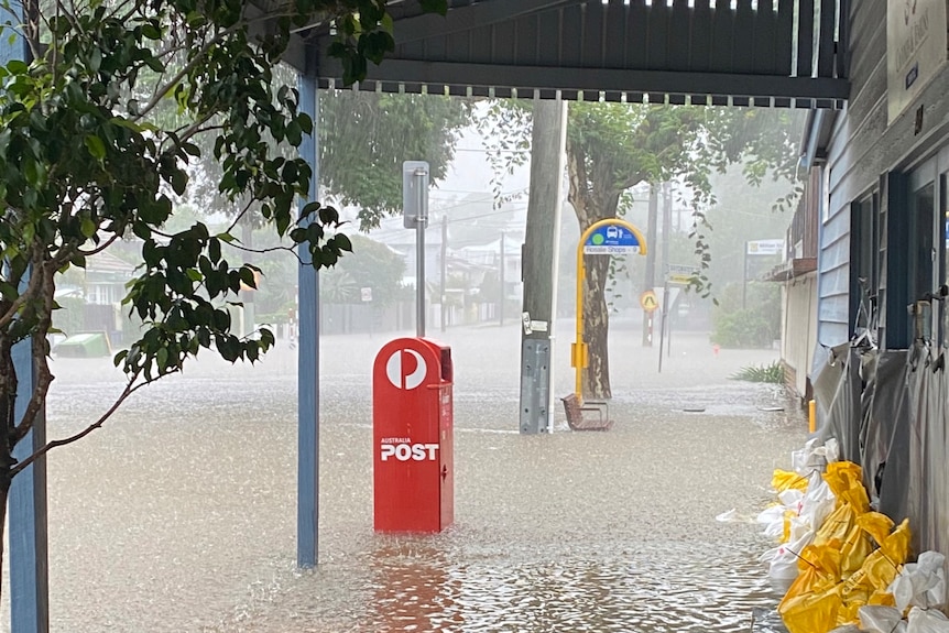 A post box sticks out above floodwaters on a shopping strip.