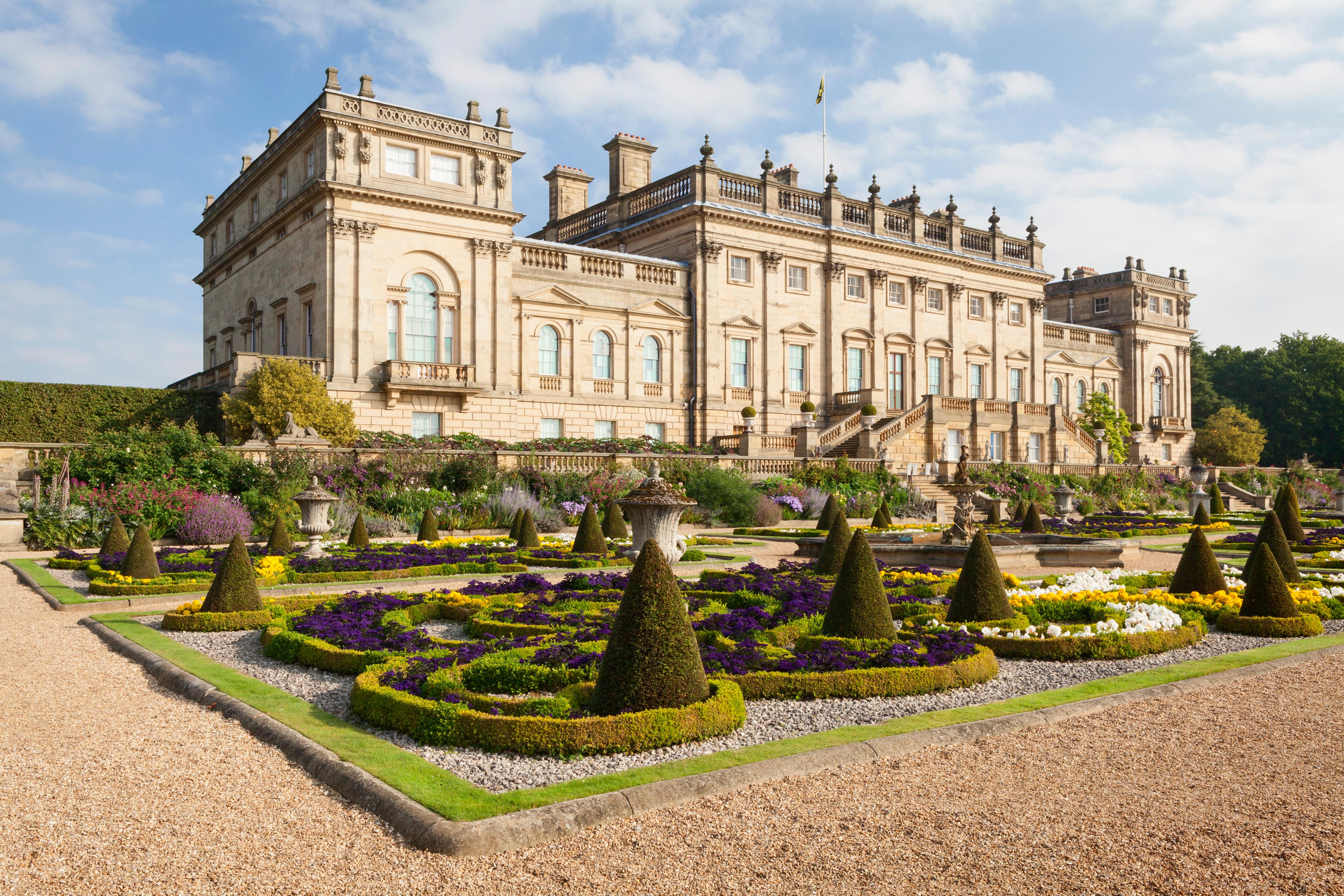 A grand, multi-story English country home, made from stone, with pillars and grand windows, including a garden with hedges 