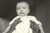 A black and white photo of a baby being held aloft.
