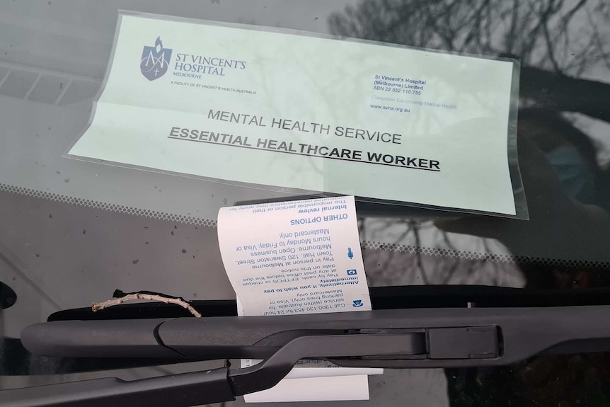 A fine under the window wiper of a car with a laminated permit on the inside that says essential healthcare worker.