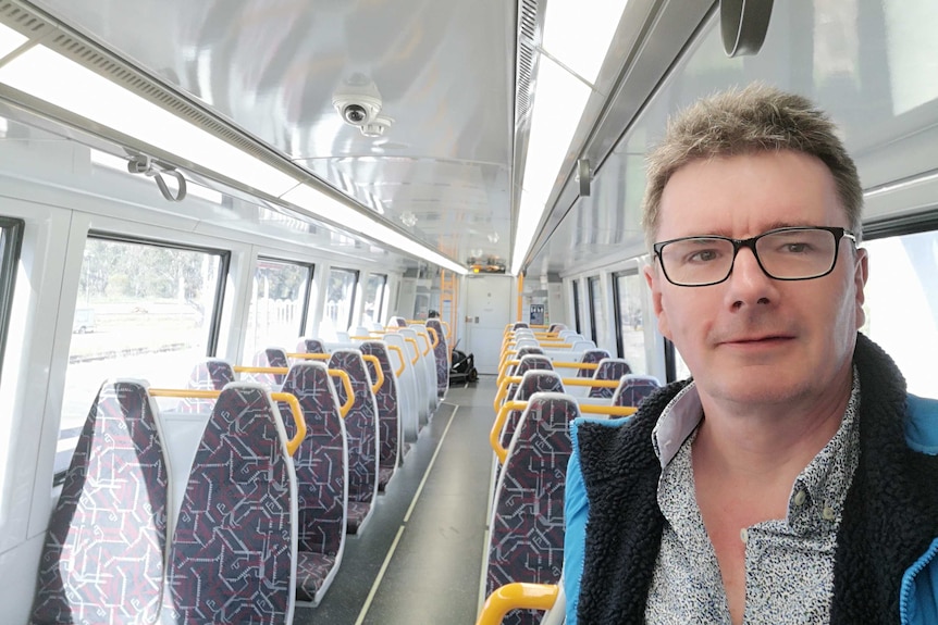 Man in glasses stands in an empty carriage on a Brisbane train