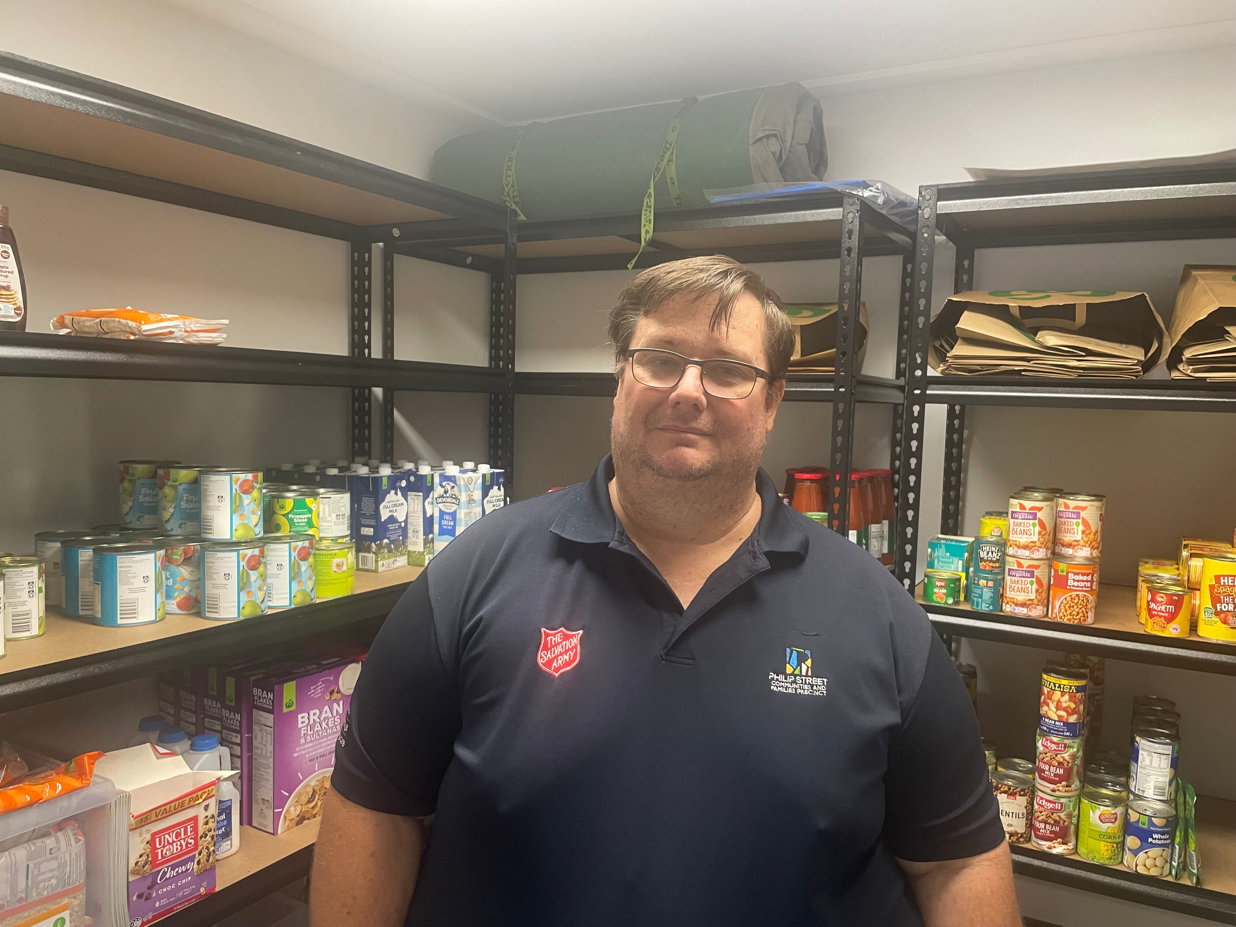 Man in blue shirt stands in front of shelves of food. 