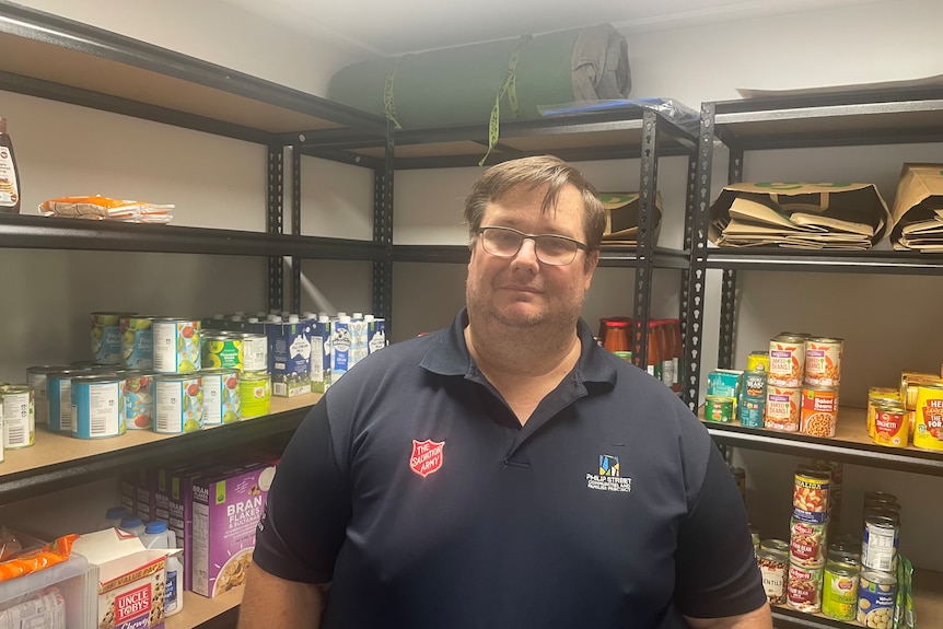 Man in blue shirt stands in front of shelves of food. 