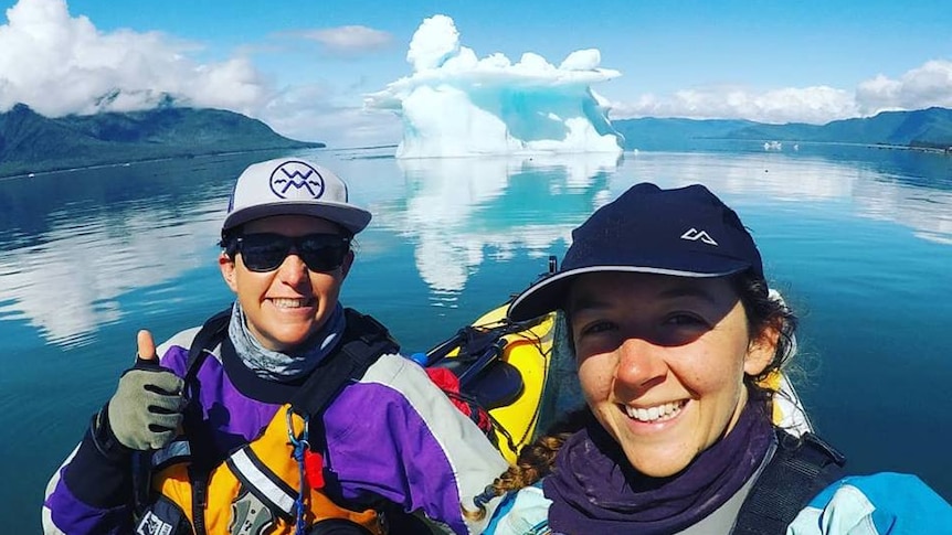 Lucy Graham and Mathilde Gordon in their kayaks with a large iceberg behind them