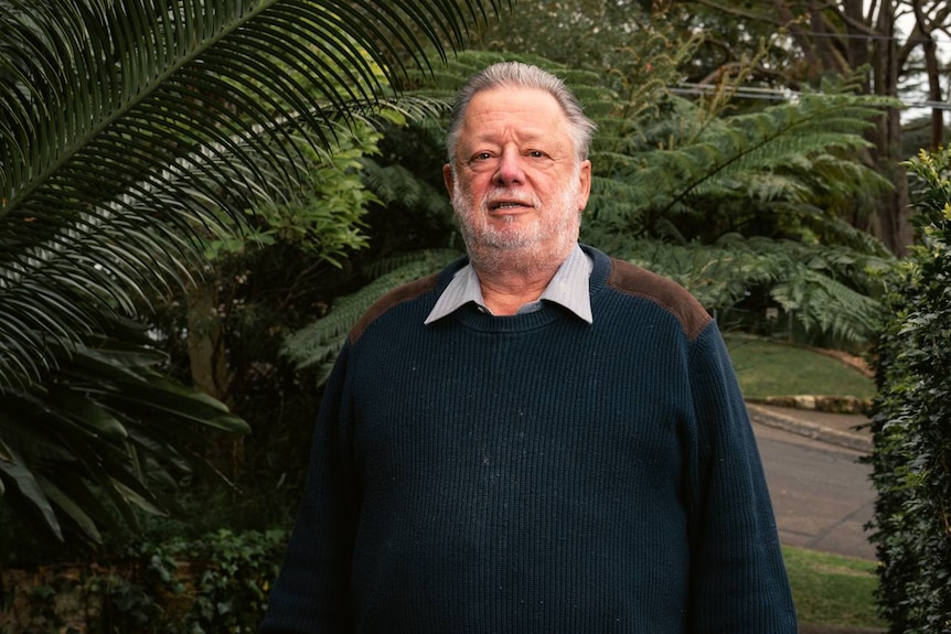 A man in a navy blue jumper stands in a garden