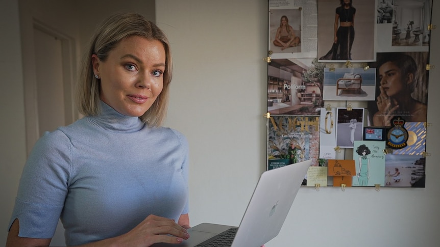 A model in a blue top holding her laptop in her home office.