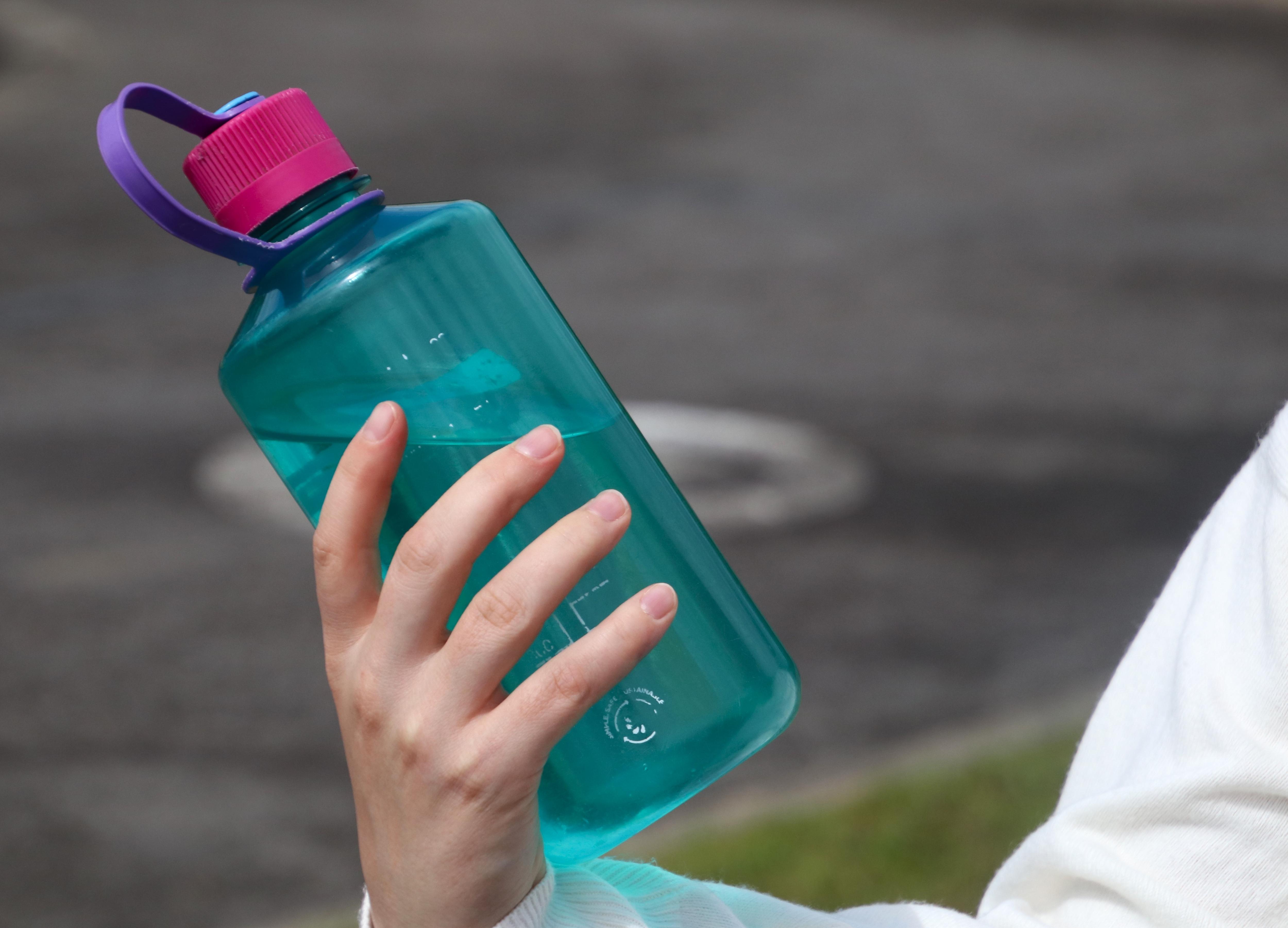 Uma pessoa segura uma garrafa de água azul reutilizável.