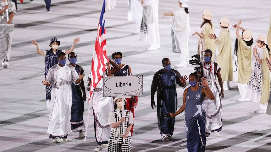 A group of athletes and officials walk with the nation's flag and behind the sign saying "Liberia" at the Tokyo Olympics.