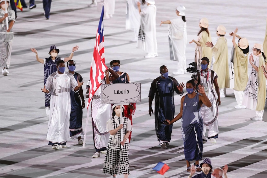 A group of athletes and officials walk with the nation's flag and behind the sign saying "Liberia" at the Tokyo Olympics.