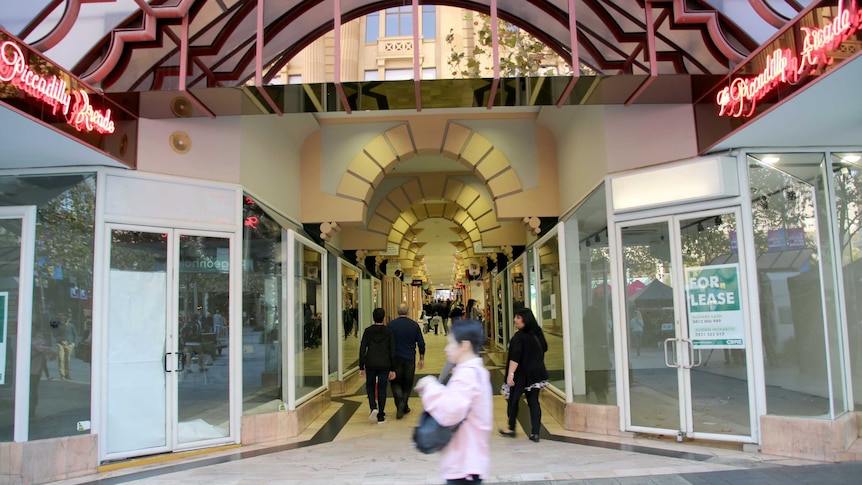 Shoppers walk past an arcade with for lease signs in the empty shop windows.