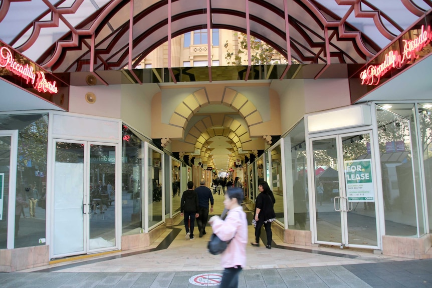 Shoppers walk past an arcade with for lease signs in the empty shop windows.