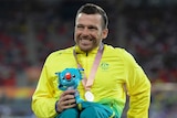 Kurt Fearnley smiles with a silver medal around his neck and a Commonwealth Games mascot in his hand.