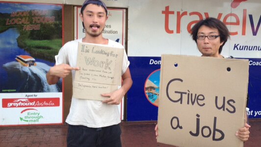 Two backpackers hold signs looking for work