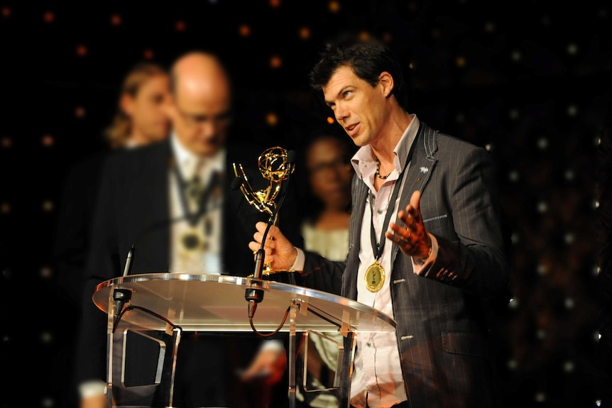 A man at a podium holding an award statue.