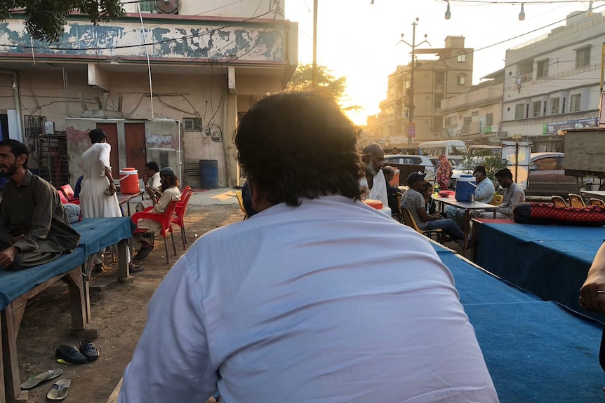 A man is shown from behind sitting at a street stall in Pakistan.