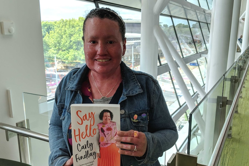 A red faced woman holds up her book with the title: Say Hello