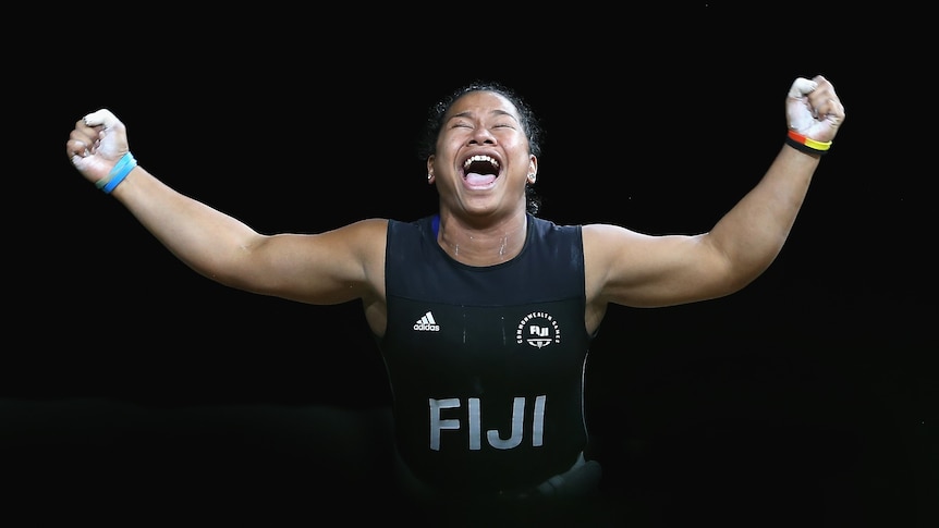 A female weightlifter raises both arms in the air and yells in celebration.