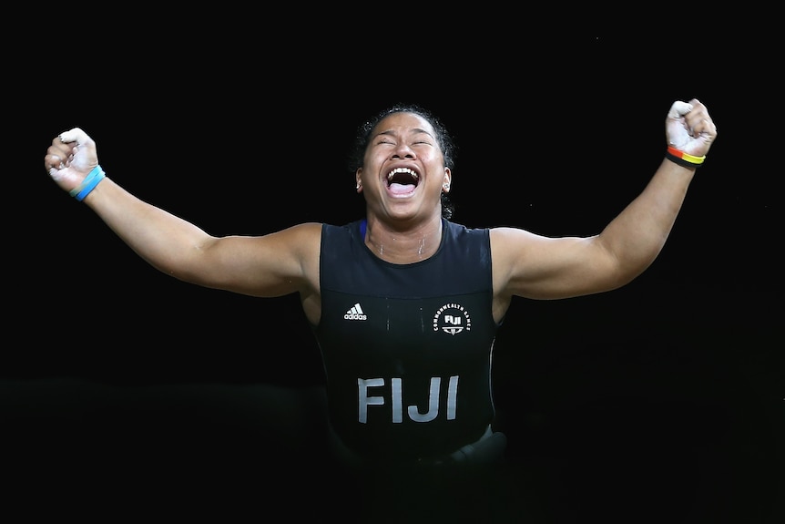 A female weightlifter raises both arms in the air and yells in celebration.